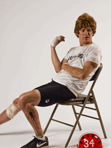 Costume guide for Dave Stoller from the movie Breaking Away.  Dave wears a white t-shirt that says Cutters on the front, a pair of bike shorts, tennis shoes, and sits on a folding chair.  There is a red bike helmet next to him with the number 34 on it.