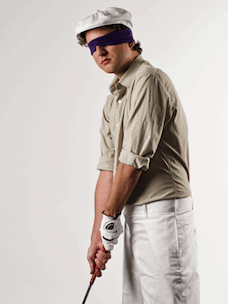 Costume guide for Ty Webb from the movie Caddyshack.  Tony wears a white newsboy cap, a beige button down shirt, and khaki pants.  He has a black blindfold and is holding a golf club.