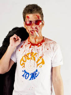Costume guide for Tyler Durden from the movie Fight Club.  Tyler has short brown hair, red sunglasses, and smokes a cigarette.  He wears a white t-shirt that says "Sock it To Me" in yellow and blue lettering.  He holds a fur jacket and his face and shirt are spattered with blood.