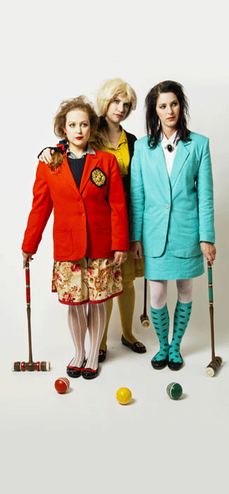 Costume guide for the three Heathers from the movie Heathers.  Red Heather wears a red blazer and a red floral skirt.  Yellow Heather wears a yellow shirt and a black jacket.  Green Heather wears a light green pants suit.  They all hold croquet mallets and have croquet balls in front of them.