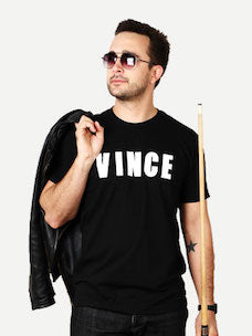Costume guide for Vince Lauria from the movie The Color of Money.  Vince has dark hair and sunglasses, he wears a black t-shirt with white lettering that says "VINCE," and dark jeans.  He holds a black jacket and a pool cue.